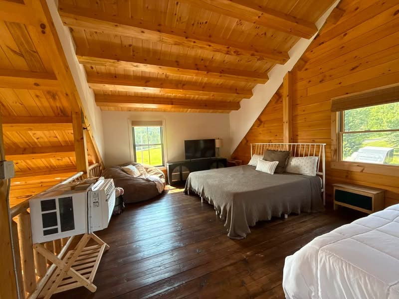 Cabin loft bedroom with a made bed under sloped pine ceilings