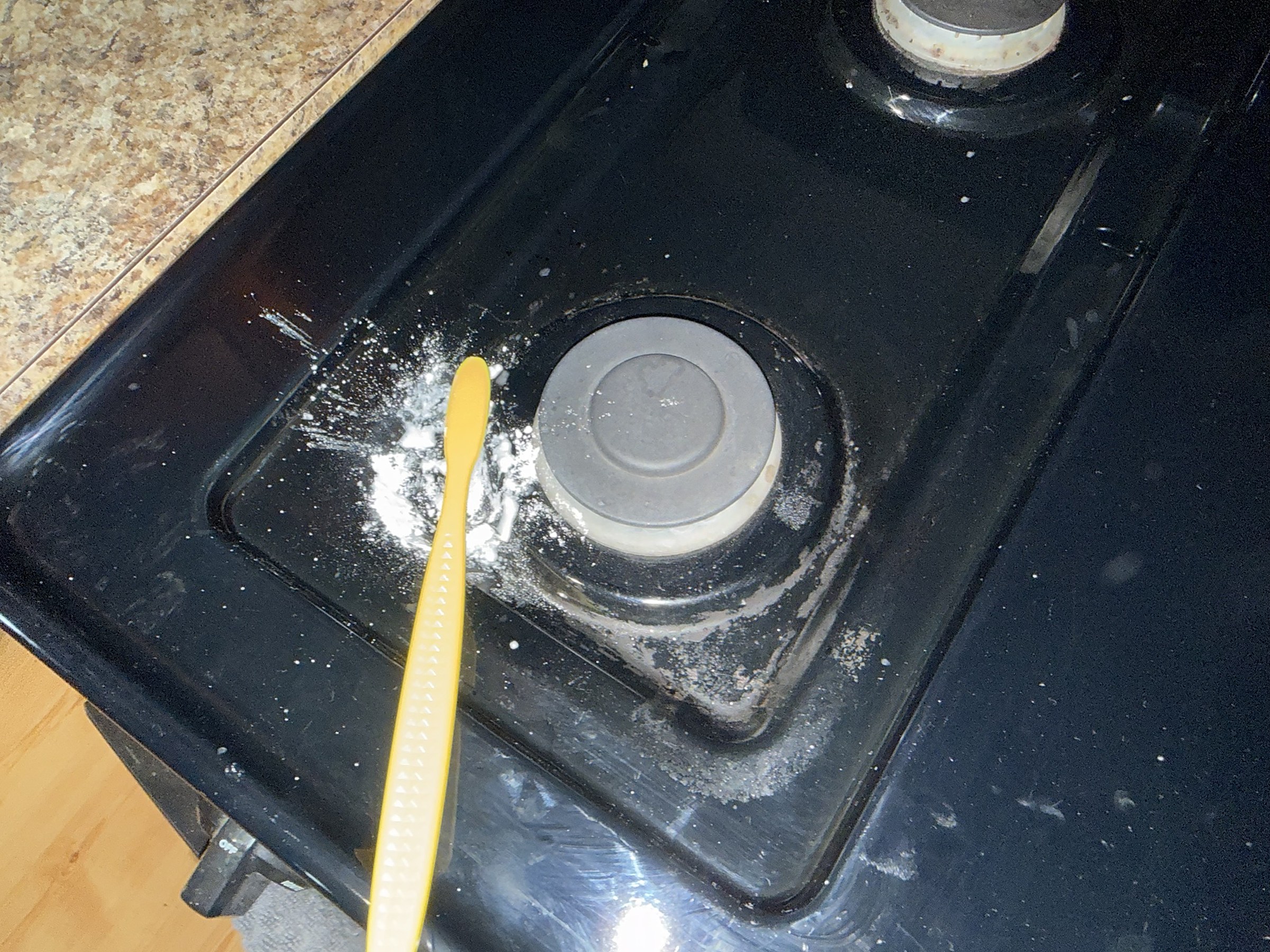During: a black gas stovetop burner being scrubbed with baking soda and a yellow brush